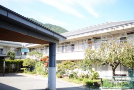施設の建物外観と入口周辺。柱と庇が特徴的な現代的な建築デザイン。